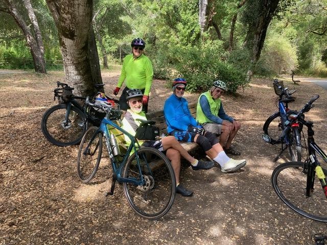 Senior Spokes riders resting on a bench along a shaded trail